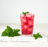 A tall glass of red berry iced tea with mint leaves and ice cubes, served on a white cutting board.